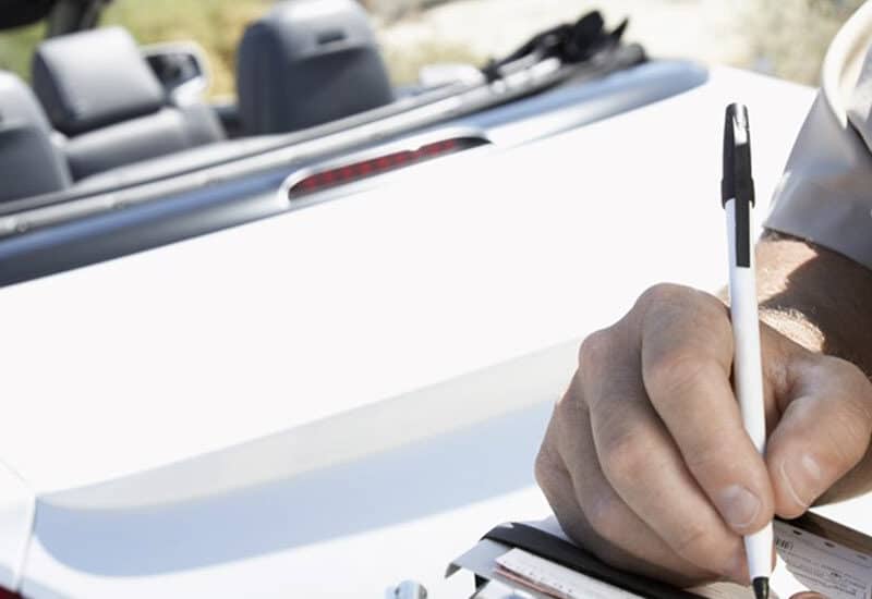 police officer writing an infringement notice to drive of a white convertible for traffic offence