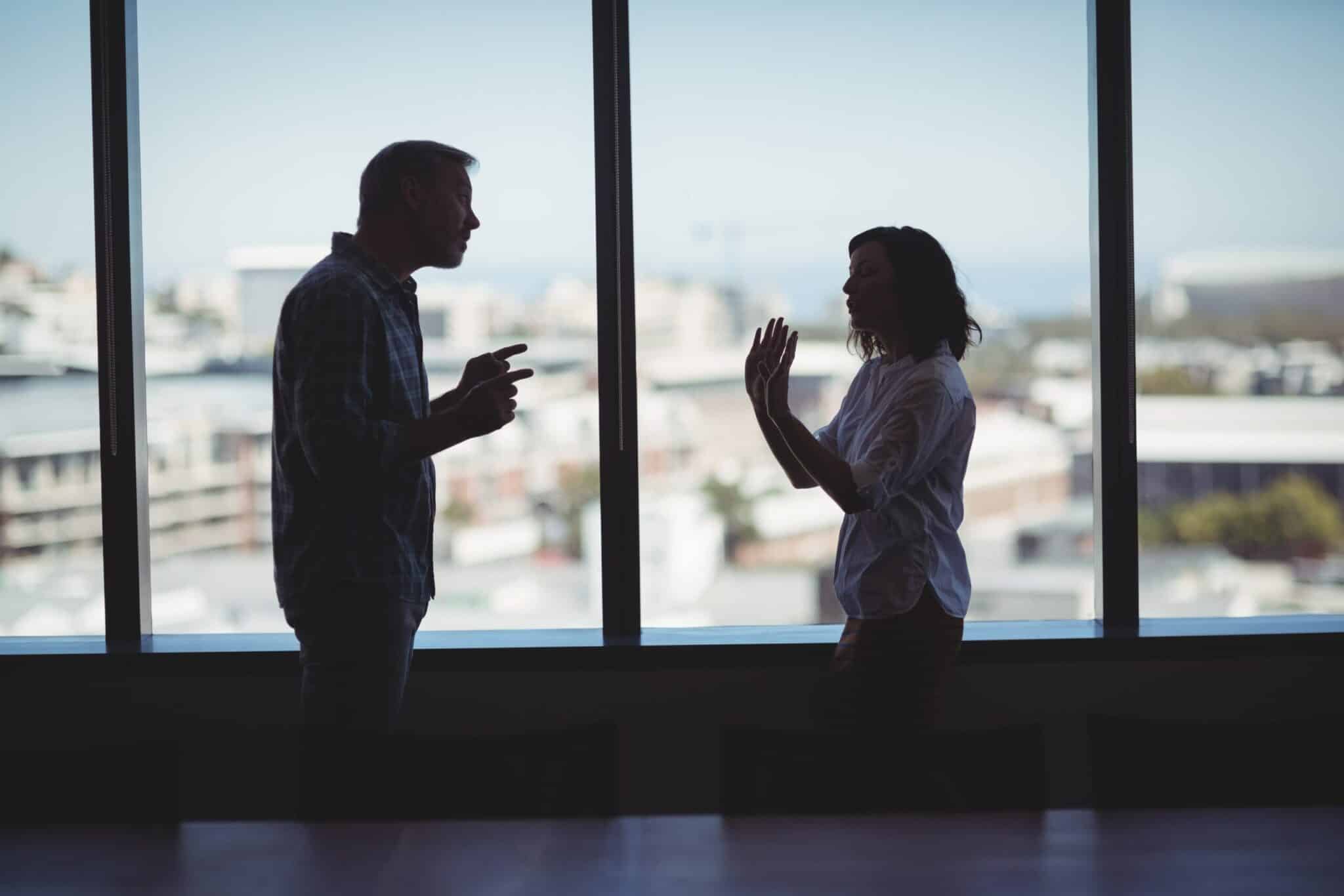 Silhouette of a couple in conflict by a window depicting domestic violence