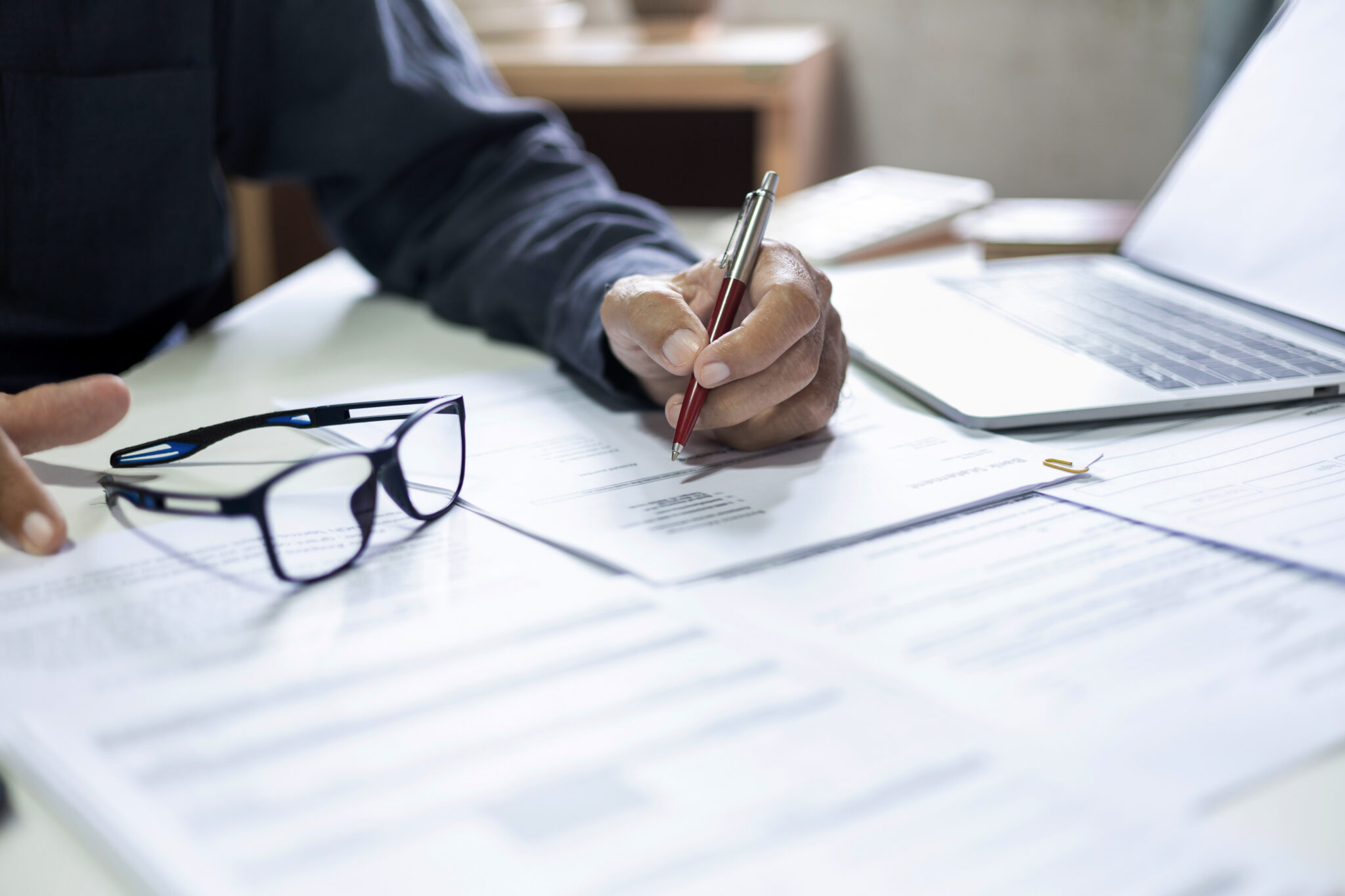 Lawyer writing on a brief with glasses and paperwork on the desk.