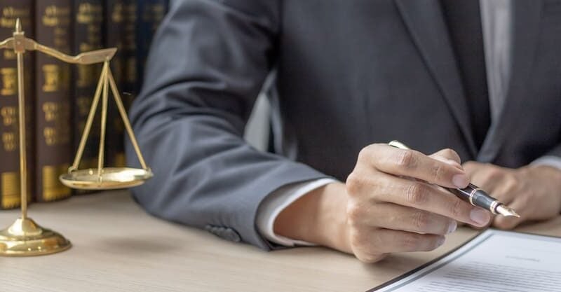 Fraud lawyer writing at a desk beside scales of justice
