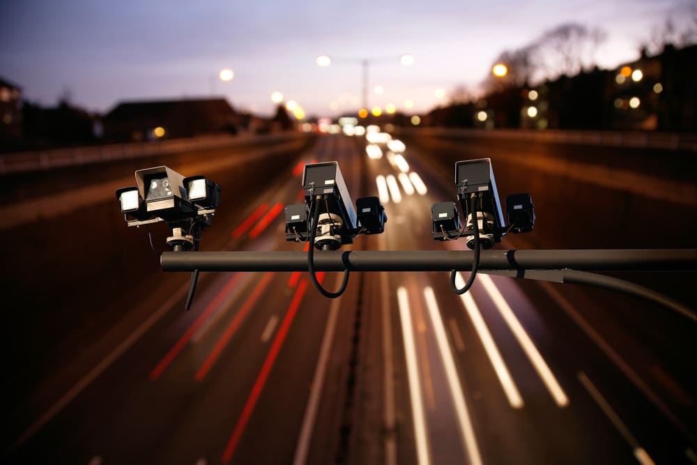 A row of three security or traffic enforcement cameras mounted on a horizontal bar overhead,